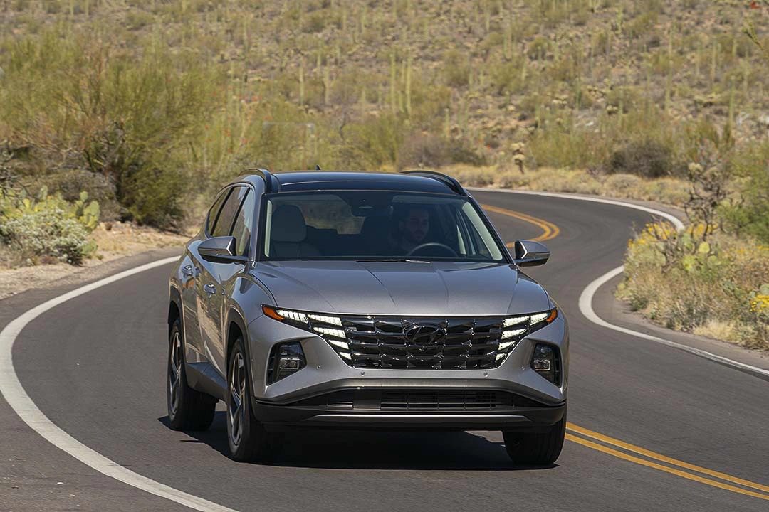 2022 grey Hyundai Tucson Hybrid driving on a winding desert road surrounded by cacti.
