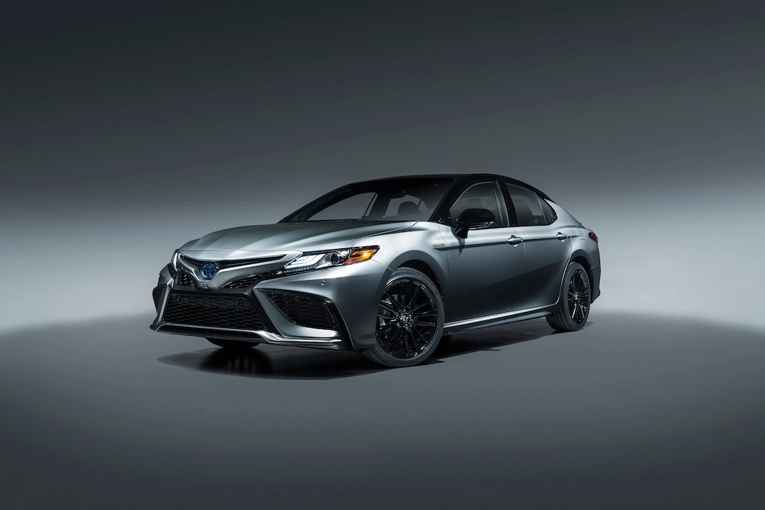 2023 dark grey Toyota Camry Hybrid XSE three-quarter front view in a minimalist studio, lighting highlighting its sporty design and black rims.
