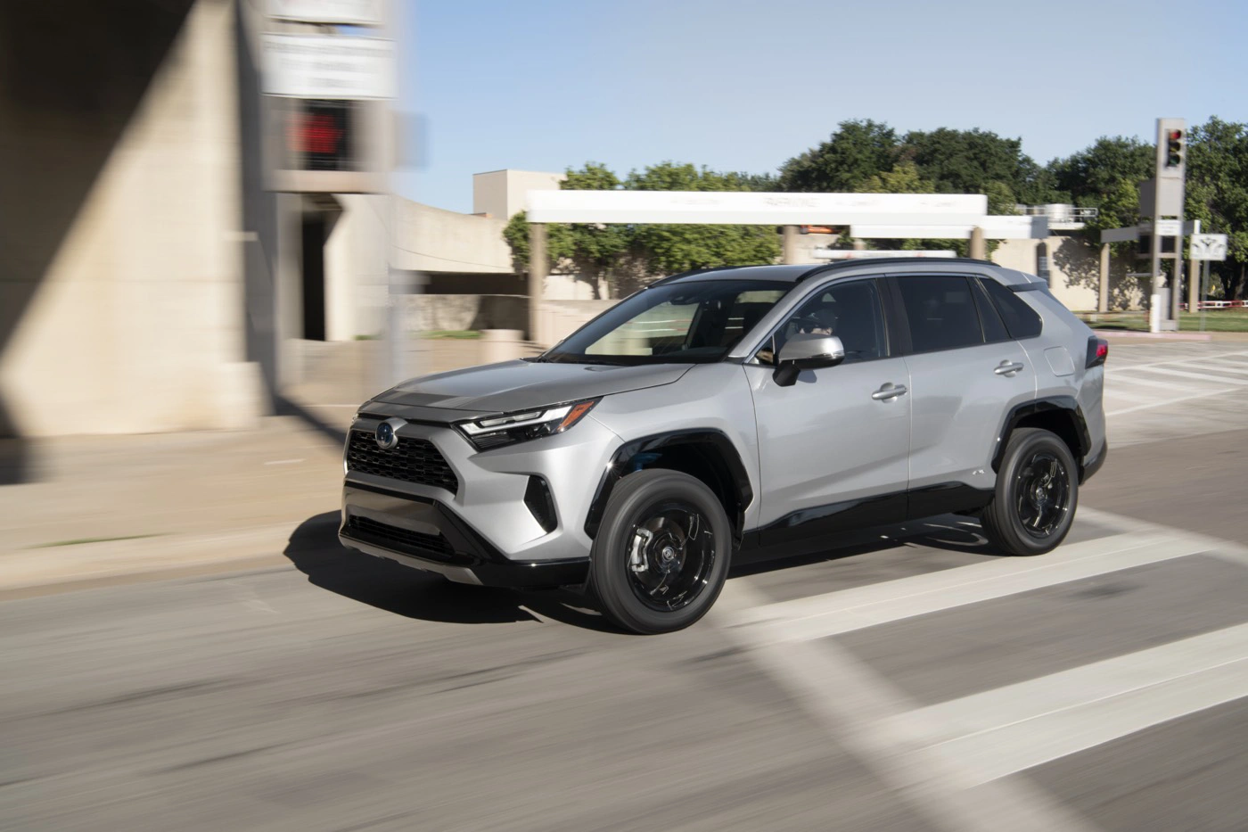 2022 silver Toyota RAV4 SE Hybrid driving in an urban setting, three-quarter front left view, city background with traffic lights visible.